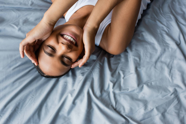 vista superior de la alegre mujer afroamericana acostada en la cama en casa - Foto, Imagen