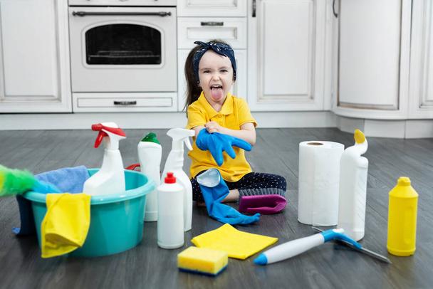 A little girl puts on gloves while cleaning the kitchen - Foto, afbeelding