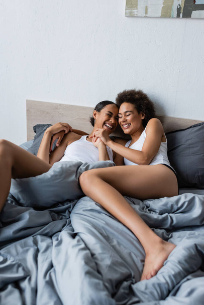 joyful and lesbian african american couple with closed eyes lying on bed at home - Zdjęcie, obraz