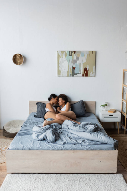 smiling lesbian african american couple hugging each other while lying in modern bedroom - Foto, immagini