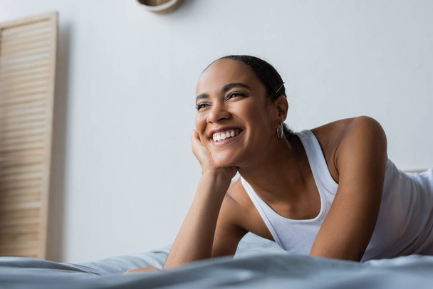 portrait of happy african american woman smiling and looking away in bedroom - Photo, image