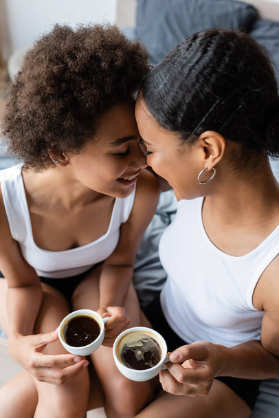 top view of cheerful lesbian african american couple holding cups of coffee  - Photo, Image