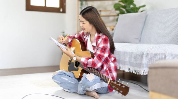 Asian woman specializes in music is composing the lyrics and melody for the opening of a new single, Using imagination and concentration in creating music, acoustic guitar, Creation of music notes. - Photo, Image