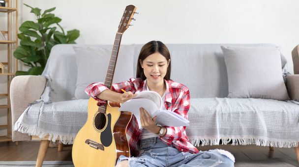 Mujer asiática especializada en música es componer las letras y melodía para la apertura de un nuevo single, Usando la imaginación y la concentración en la creación de música, guitarra acústica, Creación de notas musicales. - Foto, imagen