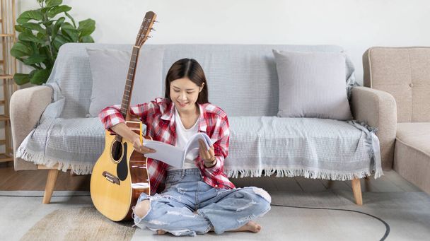 アジアの女性は音楽を専門としている新しいシングルのオープニングのための歌詞とメロディーを構成しています,音楽を作成する際に想像力と集中力を使用して,アコースティックギター,音楽ノートの作成. - 写真・画像