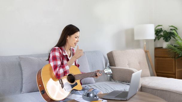 Artista mulher tocando guitarra e ao vivo ou transmitir no laptop na sala de estar, Relaxamento com musicoterapia, Fornecer prazer e entretenimento para os espectadores ou clubes de fãs, Música, Guitarra acústica. - Foto, Imagem