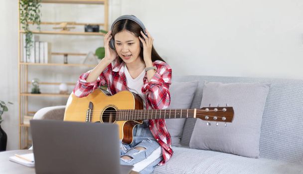Woman artist playing the guitar and live or stream on laptop in the living room, Relaxation with music therapy, Provide enjoyment and entertainment to viewers or fan clubs, Music, Acoustic guitar. - Photo, Image