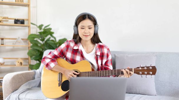 Nő művész gitározik, és élő vagy stream laptopon a nappaliban, Pihenés zeneterápiával, Szórakozás és szórakozás a nézők vagy rajongói klubok, Zene, Akusztikus gitár. - Fotó, kép