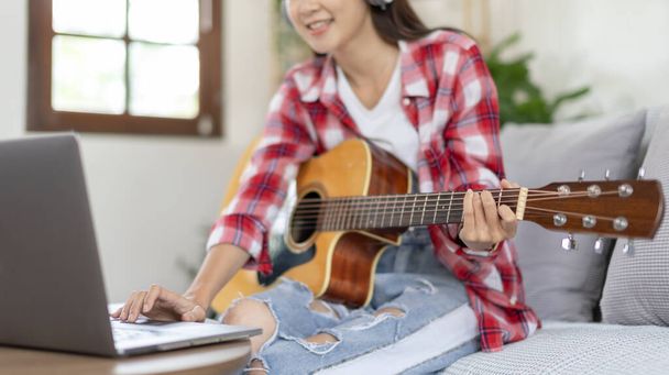 Woman artist playing the guitar and live or stream on laptop in the living room, Relaxation with music therapy, Provide enjoyment and entertainment to viewers or fan clubs, Music, Acoustic guitar. - Foto, Imagen