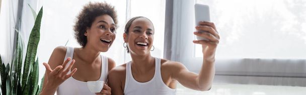 happy african american lesbian woman taking selfie with girlfriend holding cup of coffee, banner - Foto, afbeelding
