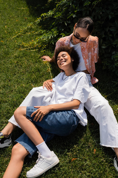 high angle view of stylish african american lesbian woman in sunglasses looking at happy girlfriend in park - Foto, Imagem