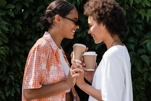 joyeuse africaine américaine lesbienne dans des lunettes de soleil tenant la main avec petite amie souriante - Photo, image