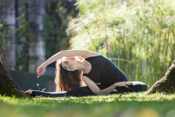 Гарненька жінка робить йогу на відкритому повітрі - сидить на розщепленнях і нахиляється в сторону. Середній постріл
 - Фото, зображення