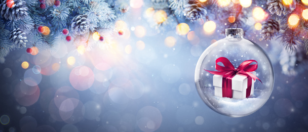 Regalo de Navidad regalo en bola colgando rama de abeto con luces Bokeh en noche de víspera abstracta azul - Foto, imagen