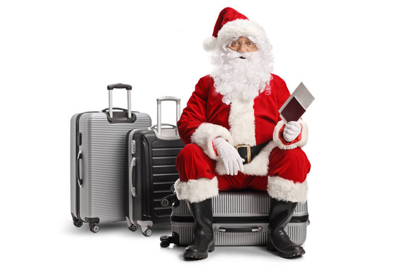 Santa claus sitting on a suitcase and holding a passport isolated on white background - Foto, Imagem