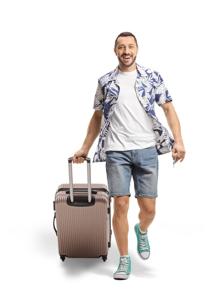 Full length portrait of a smiling man walking and pulling a suitcase isolated on white background - Photo, image