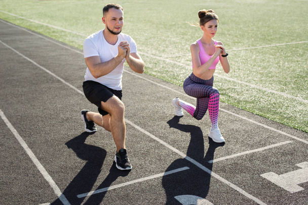 Man and a woman play sports at the stadium in the summer, making lunges - 写真・画像