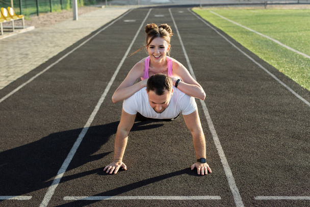 Loving couple trains together at the stadium, a man does push-UPS and a girl lies on his back - Foto, immagini