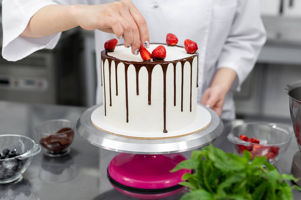 Pastry chef decorates the cake with chocolate streaks of strawberries. - Foto, imagen