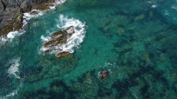 Rocas negras cubiertas de musgo entre las olas turquesas del Mar Céltico. Espuma marina blanca en las olas. Aguas del Océano Atlántico. - Foto, imagen