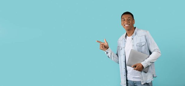 青い背景、スタジオに隔離されたコピースペースでノートパソコンの指で自信を持って若いアフリカ系アメリカ人の男を笑顔。勉強、仕事、ビジネスのリモートのための専門家からの勧告とアドバイス - 写真・画像