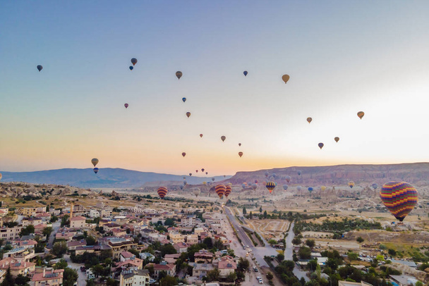 Colorful hot air balloons flying over at fairy chimneys valley in Nevsehir, Goreme, Cappadocia Turkey. Spectacular panoramic drone view of the underground city and ballooning tourism. High quality. - Foto, afbeelding