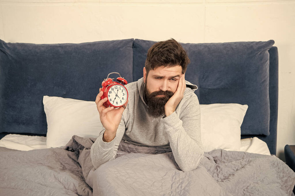 Sleepy guy holding alarm clock being in bed in morning, time. - Φωτογραφία, εικόνα