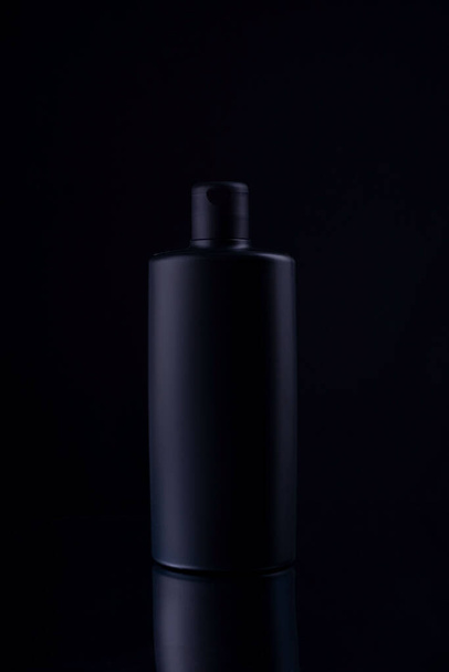 black shampoo bottle on black background still life. - Photo, image