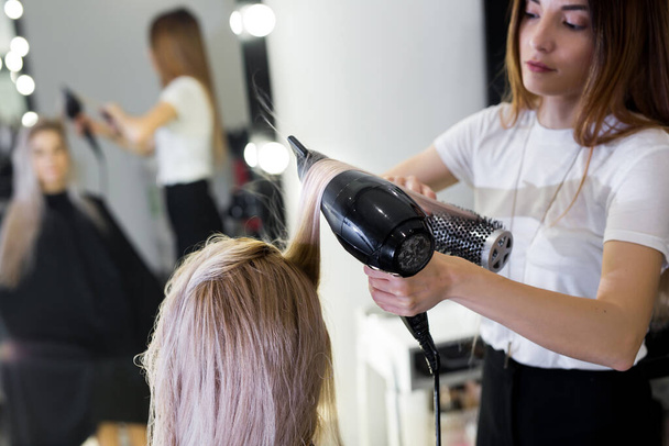 Drying long blonde hair with hair dryer and round brush. - Фото, изображение