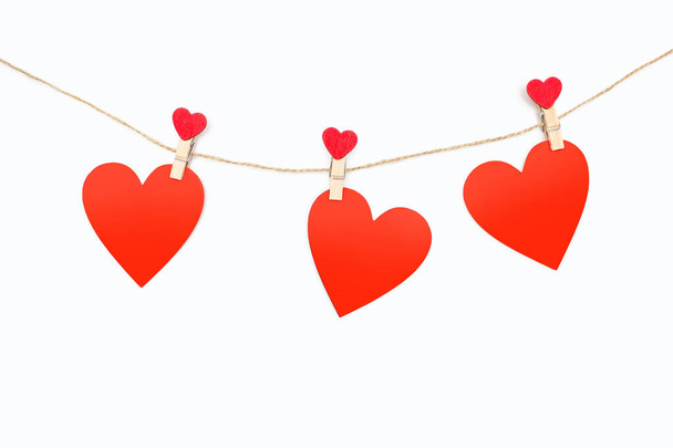 Trzy czerwone serca są przymocowane do liny z szpilkami na białym tle. Piękny wystrój w postaci serc lub dekoracji na Walentynki. Wolne miejsce na tekst - Zdjęcie, obraz