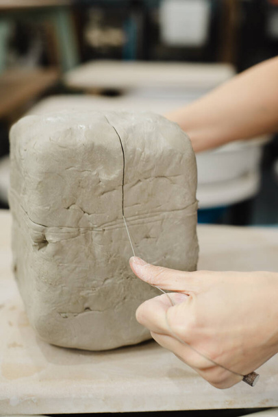Поттер режет глину проволочным резаком в керамической студии в Сиэтле, штат Вашингтон. Высококачественное фото. Секционирование глины. - Фото, изображение