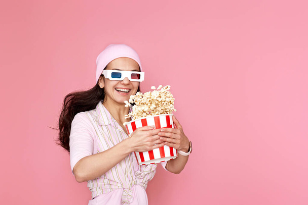 Cheerful happy woman in 3d glasses, hat holding bucket of popcorn and jumping isolated on pastel pink background. - Фото, зображення