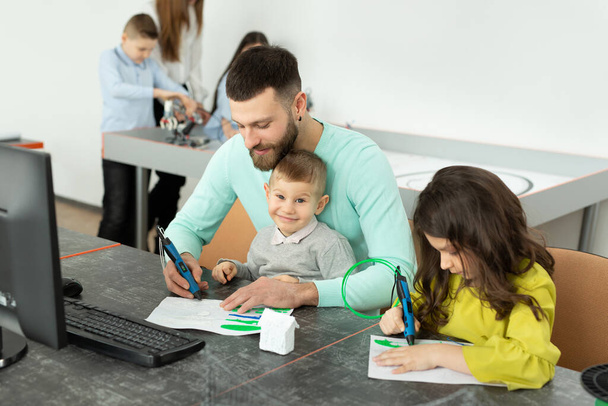 Young father with his son and daughter draw a drawing using a 3D pen in robotics classes - Foto, Bild