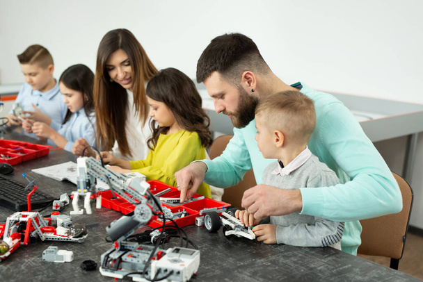 Familia con niños en un club de robótica hace un robot controlado desde un constructor - Foto, Imagen