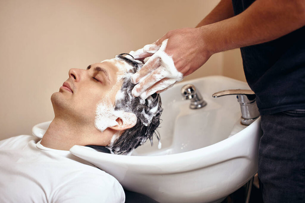 Barber washing hair of caucasian man in barber shop - Foto, Imagen