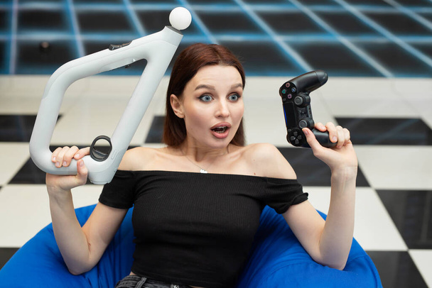An emotional woman sits in a chair and plays video games console VR with an controller - Foto, imagen