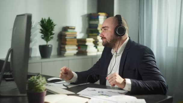 Liikemiehellä on videopuhelu kotitoimiston tietokoneella. Mies kuulokkeet toimii etänä verkossa ja on online-kokouksen kautta web-kamera. Laadukas 4k kuvamateriaalia - Materiaali, video