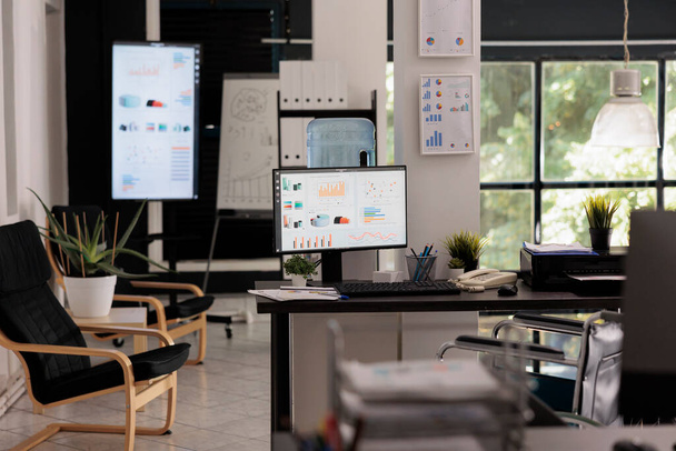 Werkruimte voor financieel analysebedrijf met desktopcomputers en groot digitaal scherm met presentatie voor analytische personeelsvergadering, kantoorrolstoeltoegankelijk concept. - Foto, afbeelding