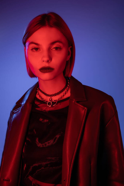 young woman in leather jacket looking at camera in red neon light on blue background - Fotografie, Obrázek