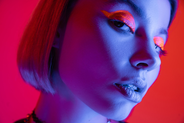 close up portrait of woman with glowing neon makeup on red and pink background - Фото, изображение