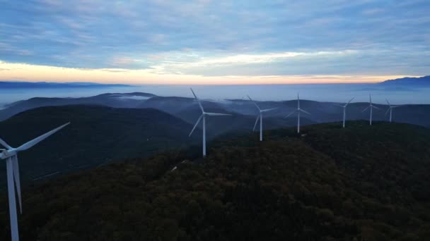 Turbinas eólicas en las montañas durante el amanecer y espesa niebla matutina en el valle. Parque eólico que produce energía verde. - Imágenes, Vídeo