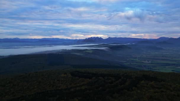 La niebla matutina atrapada en el valle fluye hacia el otro lado de la montaña. Vista panorámica de los Alpes franceses por la mañana. Central eólica en espesa niebla en la distancia - Metraje, vídeo