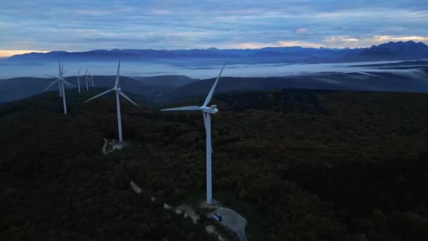 Turbinas eólicas en las montañas durante el amanecer y espesa niebla matutina en el valle. Parque eólico que produce energía verde. - Metraje, vídeo