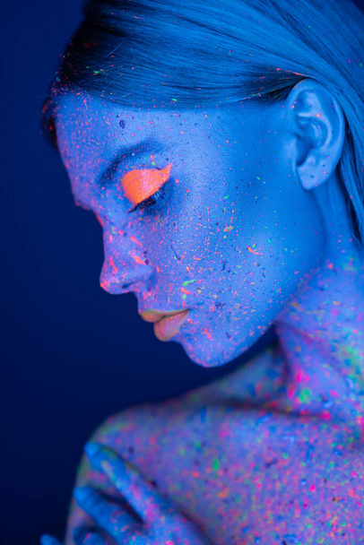 profile of woman with vibrant makeup posing in neon light isolated on dark blue - Photo, Image