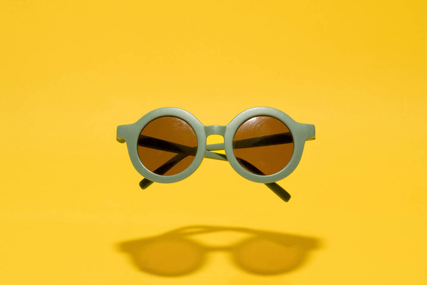 Grappig rond retro groene zonnebril voor kinderen op gele achtergrond - Foto, afbeelding