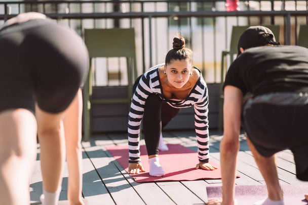 Yogi woman and diverse group of young sporty people practicing yoga, female students training at houses roof. Well being, wellness concept - 写真・画像