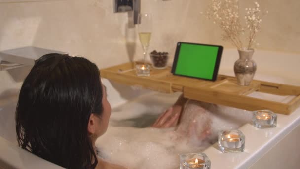 Pěkná dáma sedí v bublinkové koupeli a chatuje prostřednictvím online videohovoru. Krásná tmavovlasá žena má video chat na digitálním tabletu. Relaxační chvíle na konci dlouhého a rušného dne. - Záběry, video