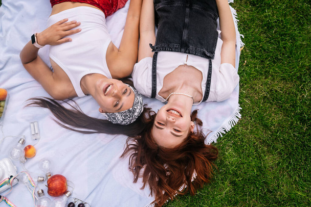 Two women having picnic together, laying on the plaid on the lawn - Foto, imagen