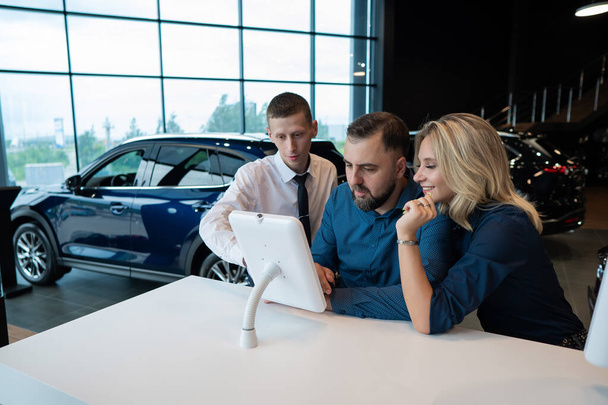 Caucasian married couple chooses a car in a car dealership on digital tablets - Fotoğraf, Görsel