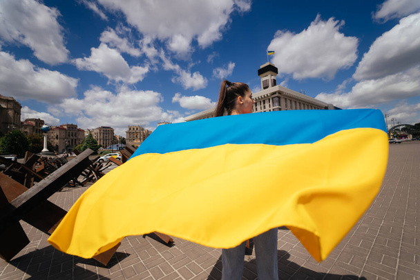A young woman carries the flag of Ukraine fluttering behind her in the street - Fotó, kép